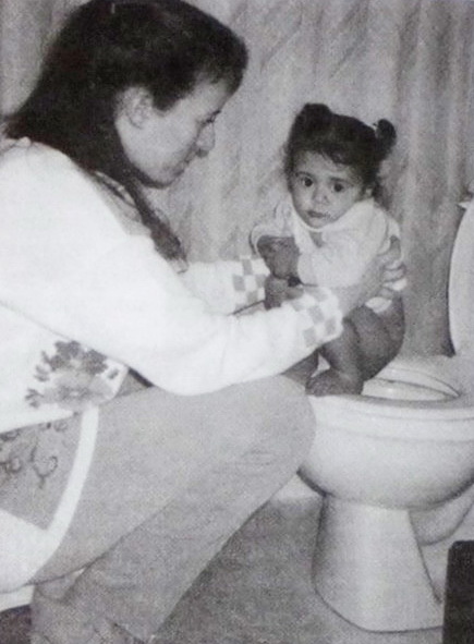 The kid sits on the toilet, and the adult in front of him