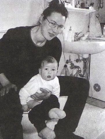The adult sits on the toilet, holding the child in front of him